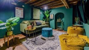 A cozy living room with a green sofa, a blue ottoman, and a yellow armchair. There is a small side table with a drink and snacks, and a large plant in the corner. - 3 Bed in Canterbury (oc-86139) (Canterbury)