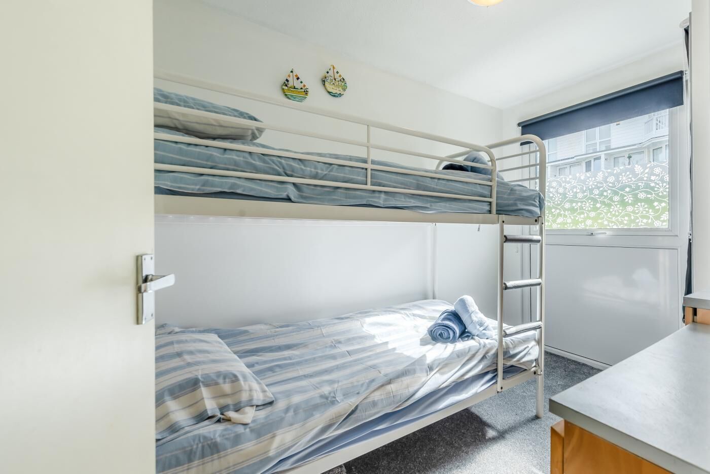 Une chambre avec un lit superposé, une fenêtre, un bureau et deux éléments de décoration murale.