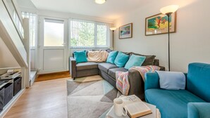 Ein modernes Wohnzimmer mit grauem Sofa, Kissen in Türkis und Weiß sowie einem blauen Sessel und einer Stehlampe.