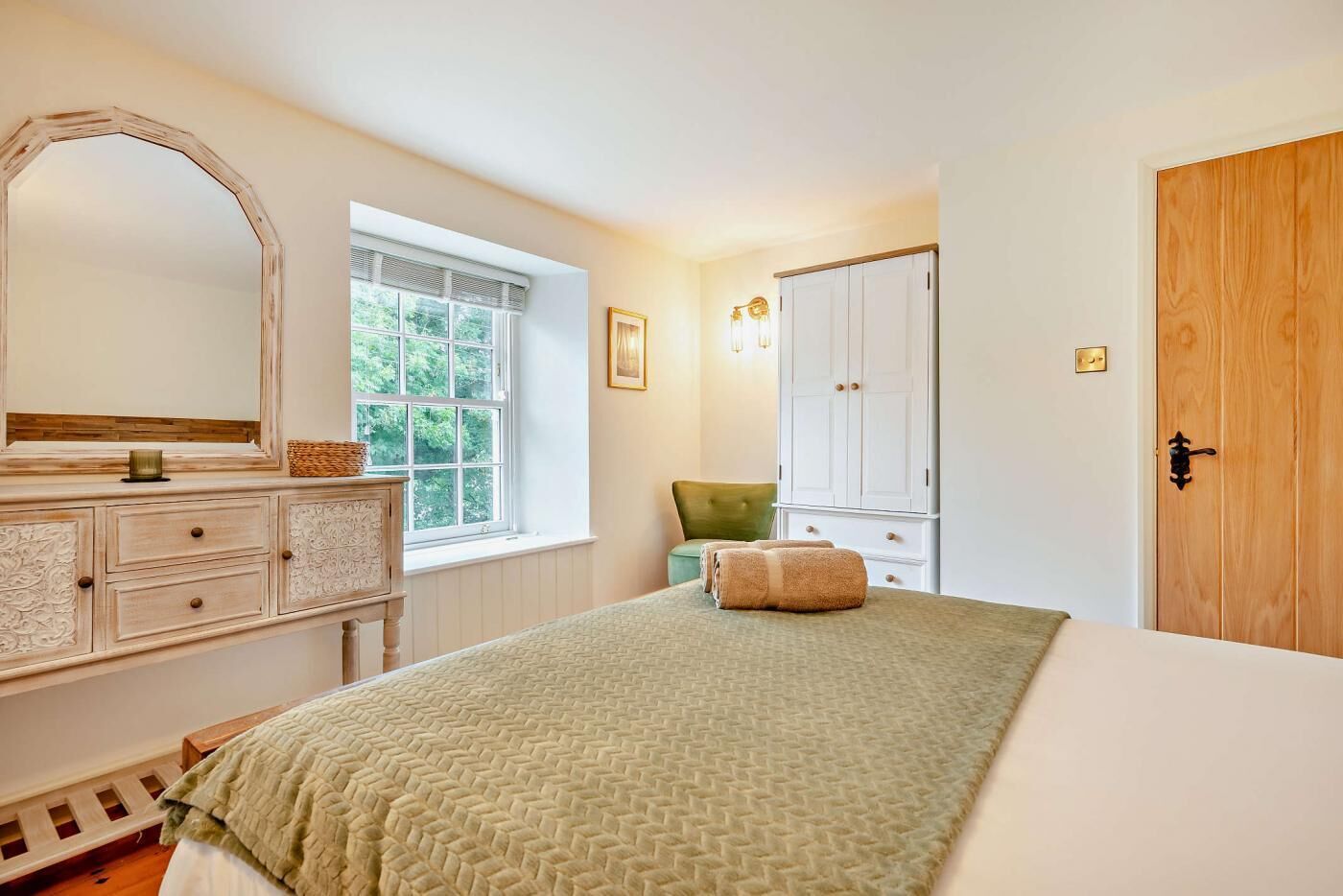 A bedroom with a large bed, a dresser, a mirror, a window, and a wardrobe.