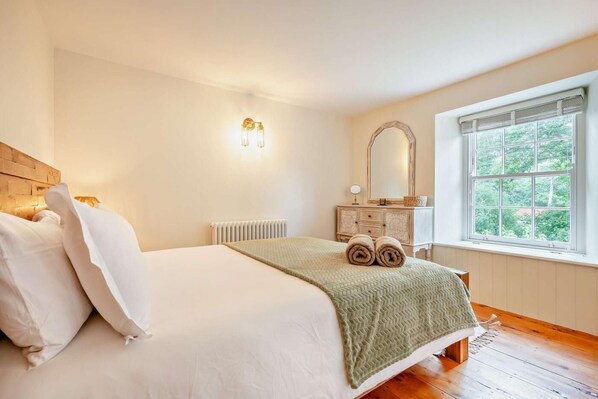 A bedroom with a bed, a dresser, a mirror, a radiator, and a window with a view of greenery.