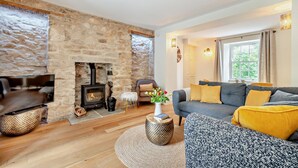 Un salón acogedor con chimenea de piedra, un sofá con cojines amarillos y un televisor sobre un mueble de madera.