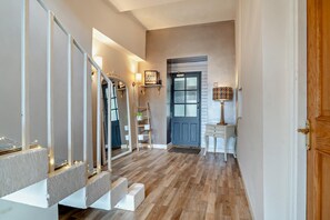A hallway with a wooden staircase, a mirror, a ladder, a door labeled 'STAGE DOOR', and a small table with a lamp.