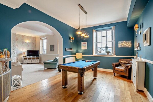 A pool table in a room with a blue wall, a television, and a seating area with a chair and a sofa.