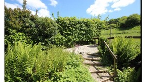 A stone staircase leading up a hill, surrounded by lush greenery and a clear blue sky. - 3 Bed in Axmouth (oc-t28930) (Axmouth)