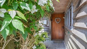 Una porta de fusta amb una decoració en forma de cor, un estri de porta i una petita finestra amb persianes.