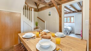 Taula de dinar de fusta preparada amb articles per a l'esmorzar, plats blancs i gots de suc d'aranja en una habitació amb bigues de fusta a la vista i una escala.