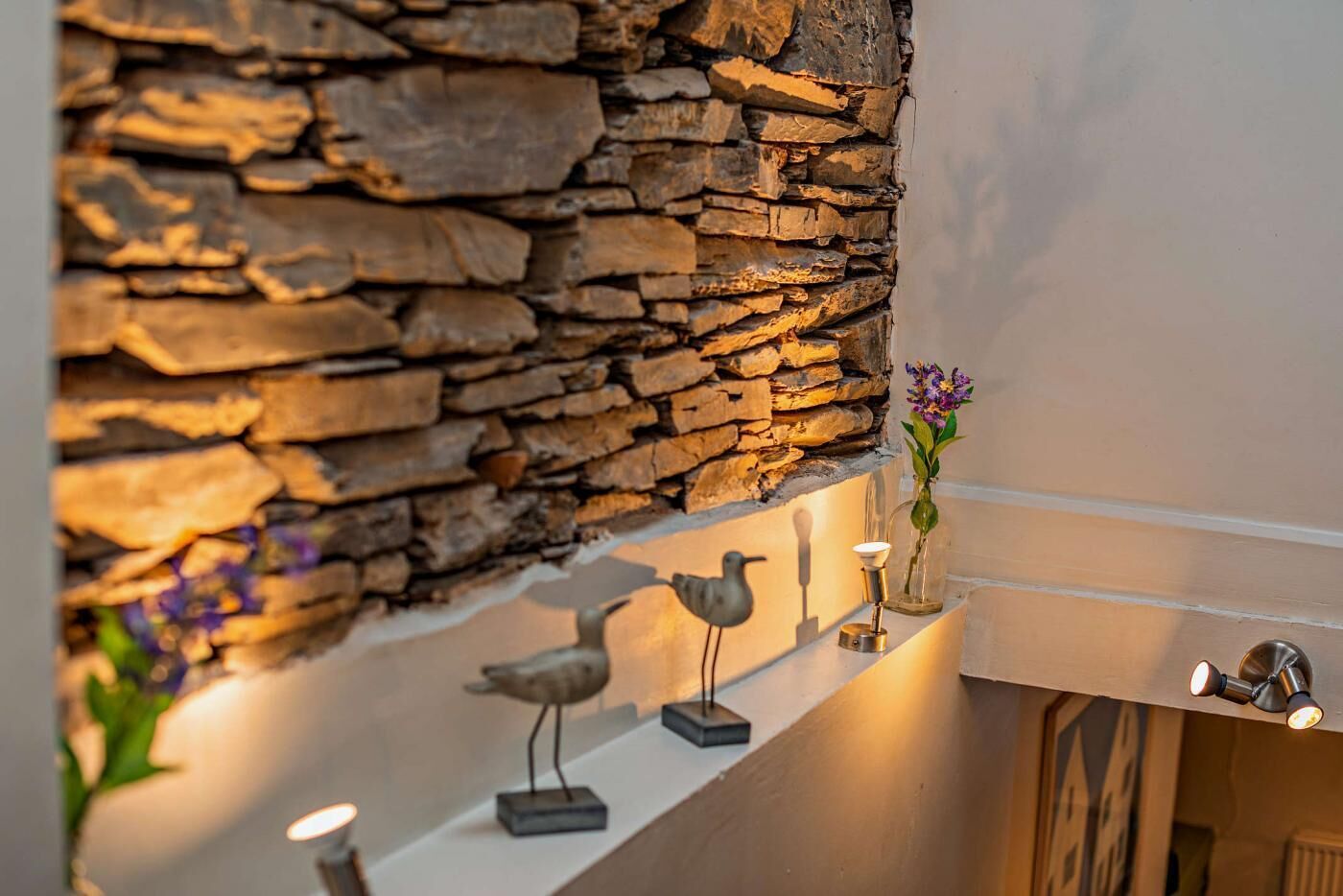 A stone wall with a shelf holding decorative items and a vase with flowers.