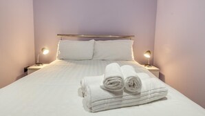 A neatly made bed with white linens and rolled towels, two bedside lamps, and a metal headboard. - 1 Bed in Tenby (oc-w28984) (Tenby)