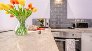 A modern kitchen with a marble countertop, a bread loaf, a vase with tulips, and a tiled backsplash. - 1 Bed in Tenby (oc-w28984) (Tenby)