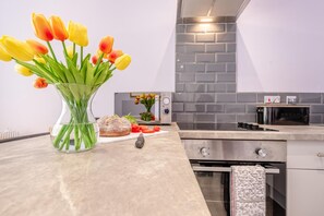 A modern kitchen with a marble countertop, a bread loaf, a vase with tulips, and a tiled backsplash. - 1 Bed in Tenby (oc-w28984) (Tenby)