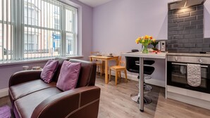 A modern kitchen with a built-in oven, a dining area with a table and chairs, and a sofa with cushions. - 1 Bed in Tenby (oc-w28984) (Tenby)