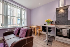 Eine moderne Küche mit Einbauofen, ein Essbereich mit Tisch und Stühlen sowie eine Couch mit Kissen.