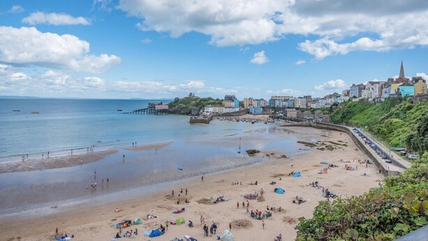 Uma vila costeira com uma praia arenosa, um cais e edifícios coloridos ao longo da costa.
