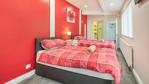 A hotel room with two beds, red walls, a painting, a TV, and a window. - 2 Bed in Tenby (oc-b28989) (Tenby)
