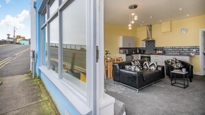 A modern apartment with a large window, a kitchen with a black and white tiled backsplash, a black leather sofa, and a dining area. - 2 Bed in Tenby (oc-b28989) (Tenby)