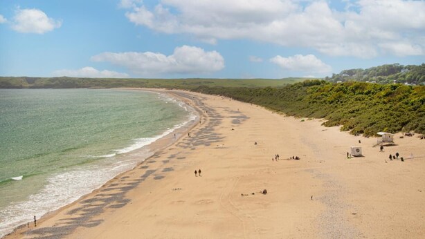 A wide sandy beach with gentle waves, a clear sky, and a distant green landscape. - 2 Bed in Tenby (oc-b28989) (Tenby)