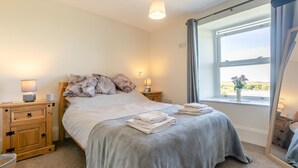 Un letto rifatto con cura, una coperta grigia, due comodini con lampade, una finestra con tende e vista sull'esterno.
