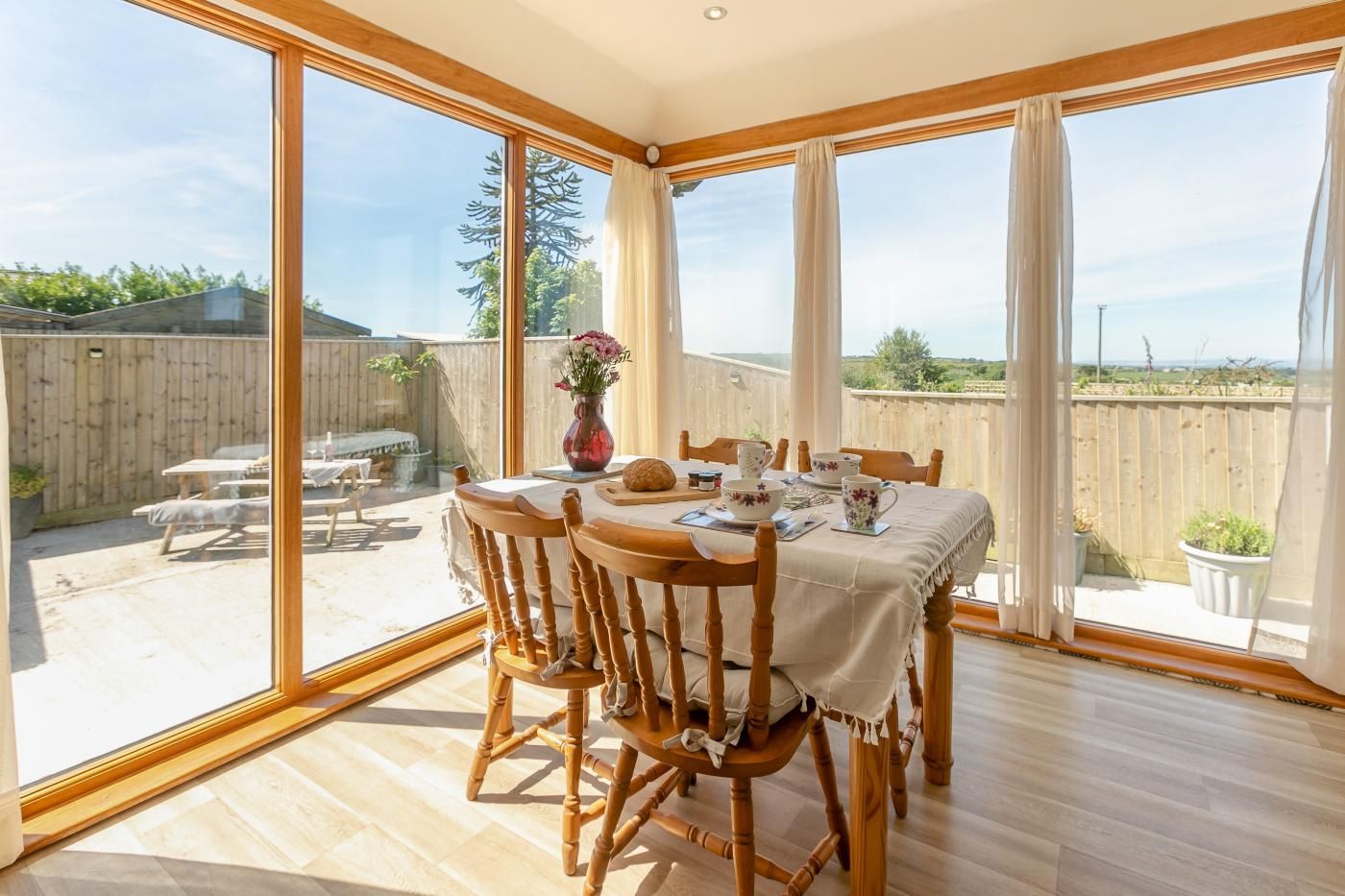 A dining area with a table set for four, wooden chairs, and a view of the backyard through large windows.