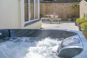 A hot tub with a wooden table and chairs in the background, surrounded by potted plants. - 1 Bed in Four Lanes (oc-f28972) (Four Lanes)