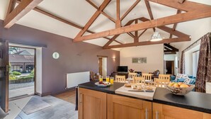 A kitchen with wooden beams, a dining area with chairs, a table with food, and a view of the outside. - 3 Bed in Thwing (oc-t29011) (Thwing)