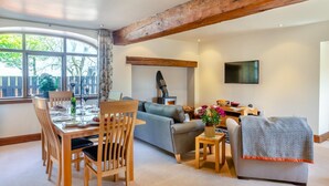 Un salón acogedor con comedor, vigas de madera, chimenea y televisor montado en la pared.