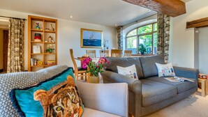 Una sala de estar acogedora con un sofá gris, un sillón estampado y una estantería de madera.