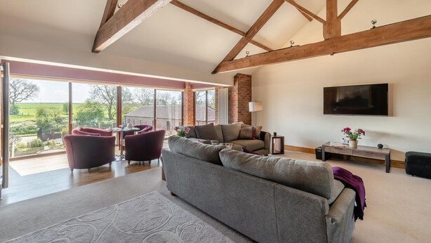 A spacious living room with a high ceiling, large windows, a grey sofa, and a flat-screen TV. - 4 Bed in Thwing (oc-t29013) (Thwing)