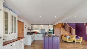A spacious kitchen with white cabinetry, a central island, and a dining area with yellow chairs. - 4 Bed in Thwing (oc-t29013) (Thwing)