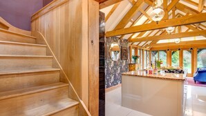 Una escalera de madera que lleva a una cocina con una isla grande, vigas de madera y vistas al exterior.