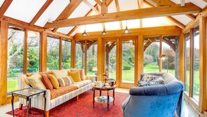 Una habitación amplia con techo alto, ventanas grandes, un sofá, un sillón azul y una pequeña mesa sobre una alfombra roja.