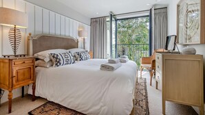 Camera d'albergo con un letto grande, lampade sui comodini, un comodino in legno, una cassettiera e un balcone con tende.