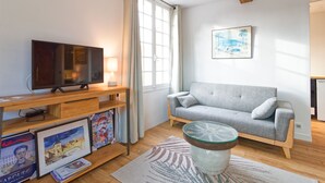 Una sala de estar moderna con un sofá gris, suelo de madera, una mesa de centro de vidrio y un televisor sobre un mueble de madera.