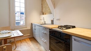 Una cocina compacta con ventana, radiador, estufa y comedor con mesa y sillas.