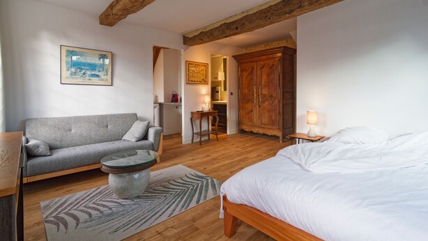 Un dormitorio con una cama de madera, un sofá gris, una mesita redonda y un armario.