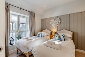 A bedroom with two beds, a heart-shaped wall decoration, and a window with curtains. - 2 Bed in Padstow (oc-t29016) (Padstow)