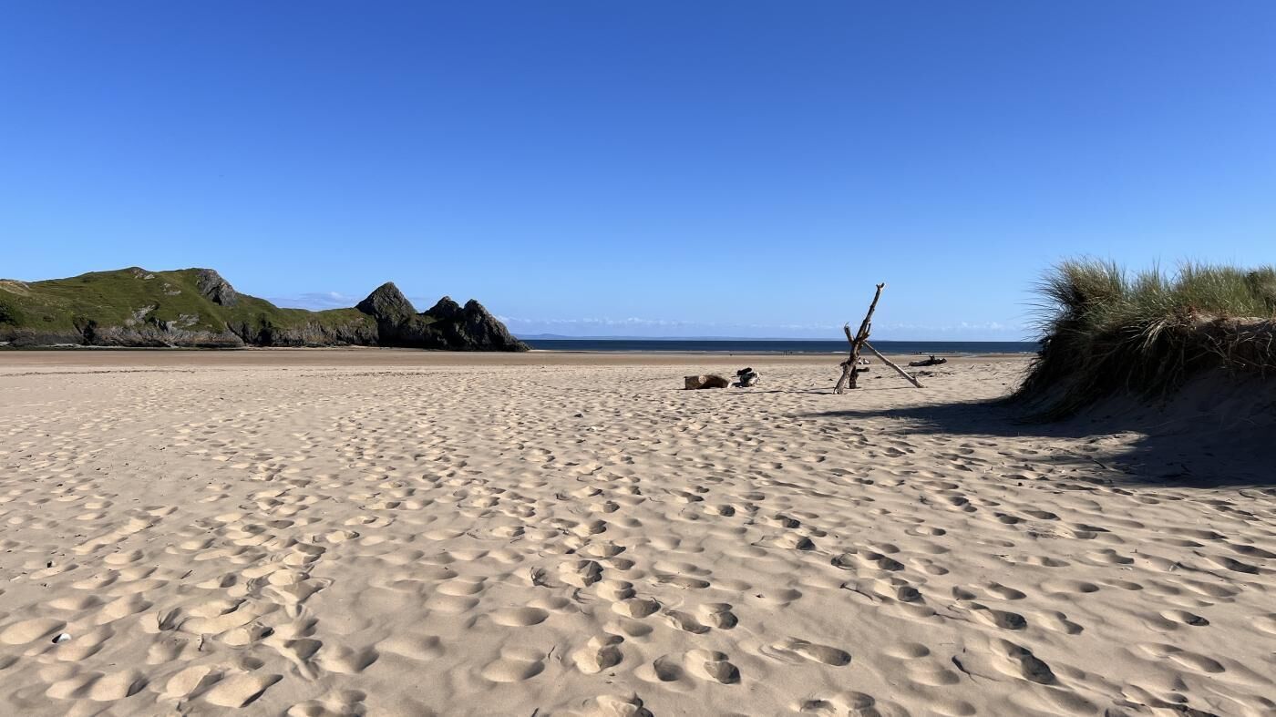 A sandy beach with footprints, a wooden structure, and grassy dunes.