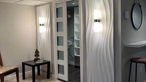 Una habitación moderna con piso de madera, una silla, una mesita con una estatua y un vestidor con puertas de vidrio.