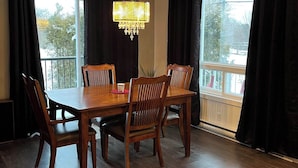Un comedor con una mesa y sillas de madera, una araña y ventanas grandes con cortinas.