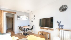 Uma sala de estar moderna com área de jantar, TV fixada na parede e janela com moldura de madeira.