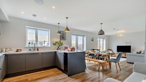 Une cuisine moderne dotée d’un îlot central, un coin repas avec une table et des chaises en bois, et un salon avec un canapé et une télévision.