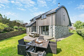 A modern house with a stone exterior, a large patio with wicker furniture, and a stone wall garden. - 3 Bed in Trevone (oc-c29020) (Trevone)