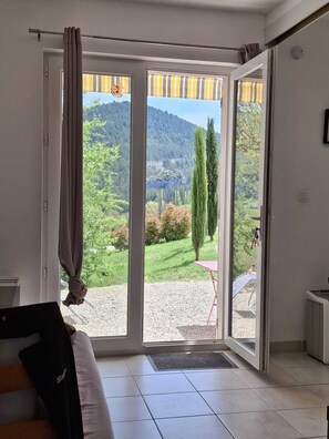 A room with a sliding glass door leading to a garden, a bed, and a small table. - Les Deux Villages n°3 - Studio avec Terrasse (Montbrun-les-Bains)