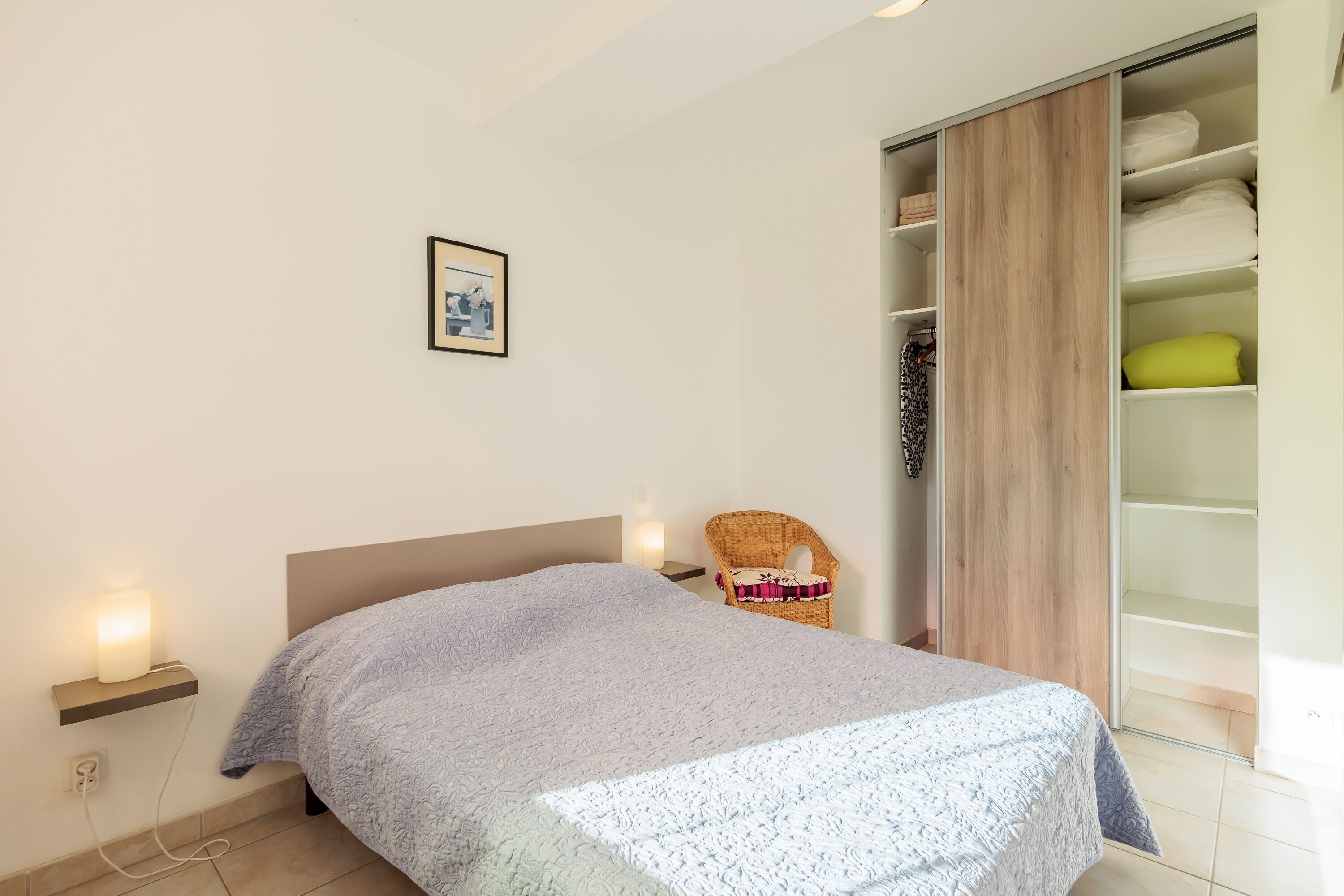 A bedroom with a bed, a chair, a wardrobe, and a wall-mounted light.