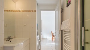 Kapea käytävä, jonka vasemmalla puolella on kylpyhuone ja oikealla puolella pesukone sekä ruokailutila, jossa on tuoleja ja pöytä.
