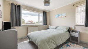 A bedroom with a bed, bedside tables, a TV, and a view of the outside. - 3 Bed in Bacton (oc-l2294) (Bacton)