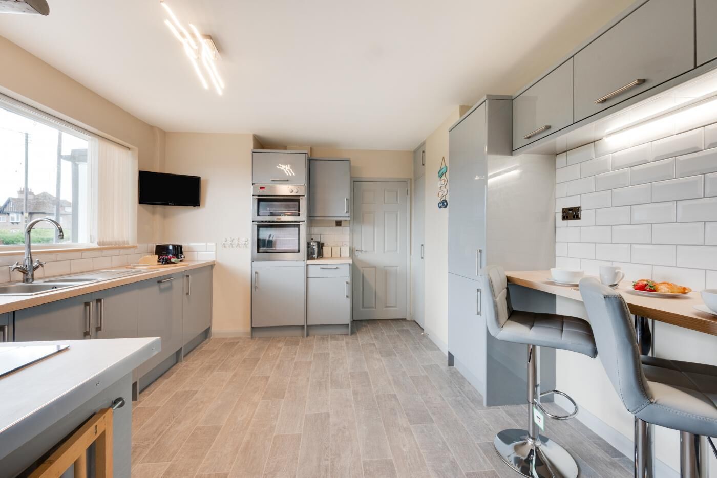 A modern kitchen with grey cabinets, a built-in oven, a refrigerator, and a dining area with a table and chairs.