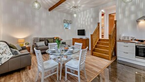 Ein modernes Wohnzimmer mit einem Glastisch, weißen Stühlen, einer Couch und einer Treppe, die zur Küche führt.