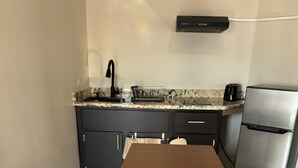 A modern kitchen with a wooden table, dark cabinets, a stainless steel refrigerator, and a countertop with a coffee maker.
