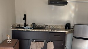 A modern kitchen with a stainless steel refrigerator, a black range hood, and a marble countertop.
